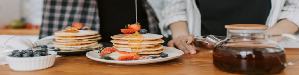 A plate of pancakes with syrup and fruit on top.