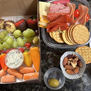 A table with two trays of food and one tray has crackers, fruit, cheese, nuts, and other items.