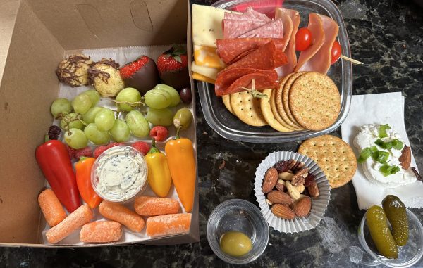 A table with two trays of food and one tray has crackers, fruit, cheese, nuts, and other items.